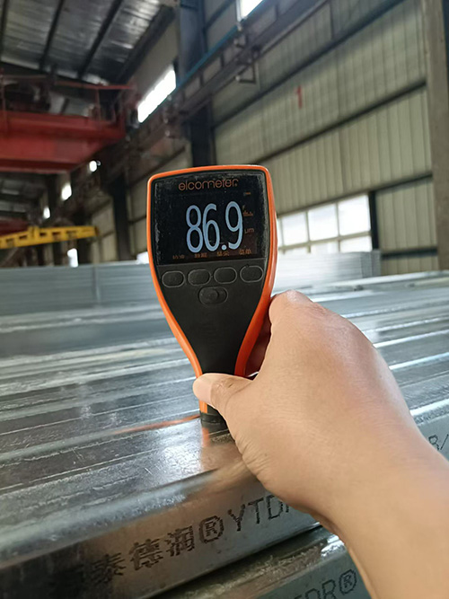 Quality control inspector measuring galvanized zinc coating thickness using digital magnetic gauge